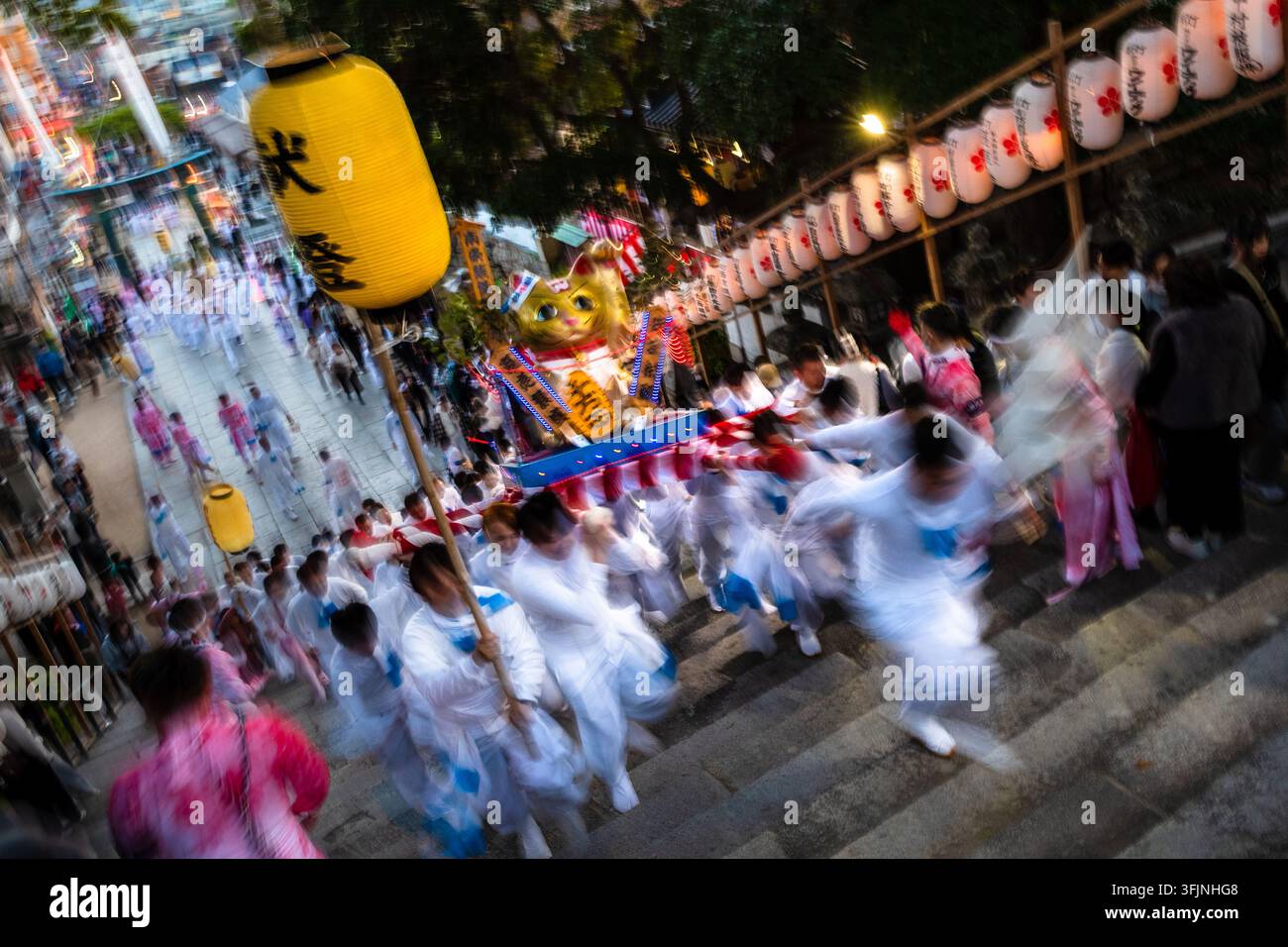 Japanische Männer in zeremonieller weißer Kleidung laufen die Treppen hinauf, während sie einen tragbaren Schrein beim Gojinko-Fest in Hofu, Japan, tragen. Stockfoto