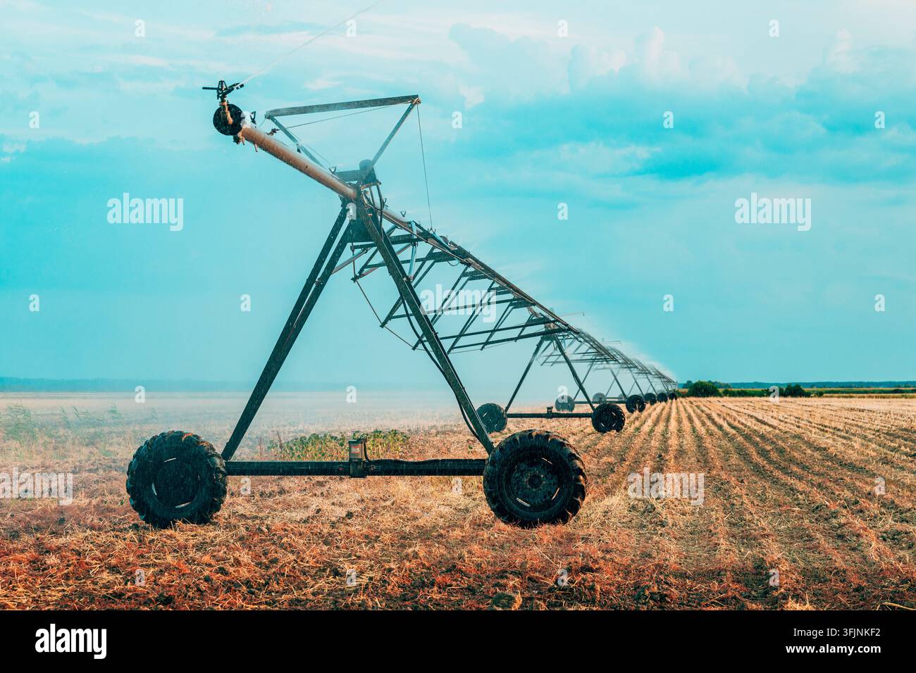 Zentralschwenkbewässerungssystem, das ein weitläufiges trockenes Feld unter einem ruhigen Abendhimmel überspannt. Moderne landwirtschaftliche Infrastruktur, effiziente Bewässerung und Stockfoto