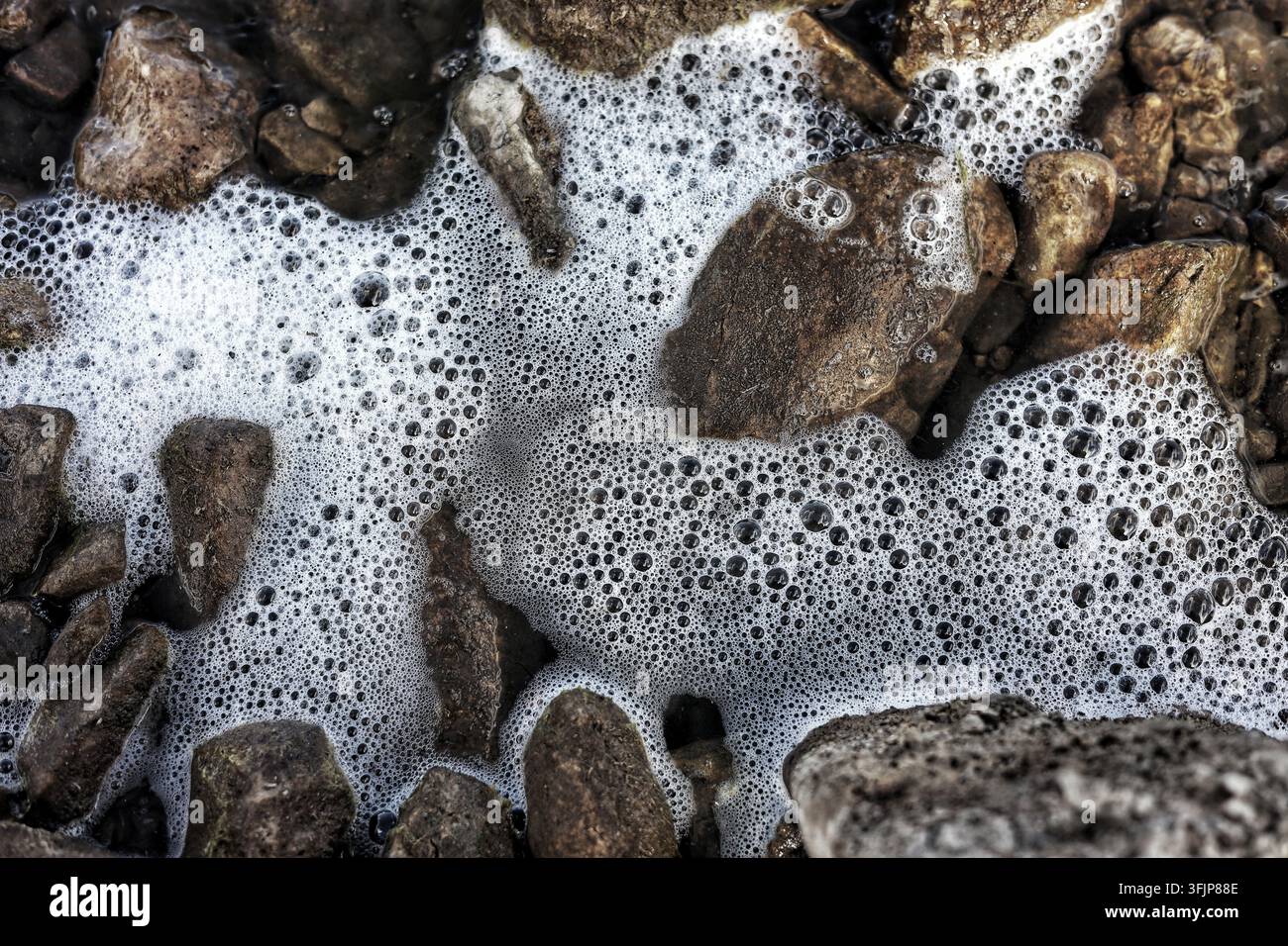 Makro-Nahaufnahme von Weißwasser-Schaum und Blasen über felsiger Seenküste Stockfoto