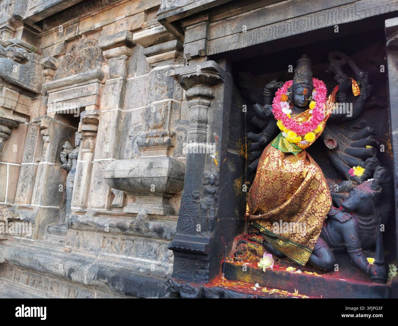 Steinskulptur einer vielarmigen Göttin, gekleidet in goldene Seide und einen Blumengirlande, in einer Nische einer Hindutempelwand in Chidambaram, Tamil Nadu, Indien Stockfoto