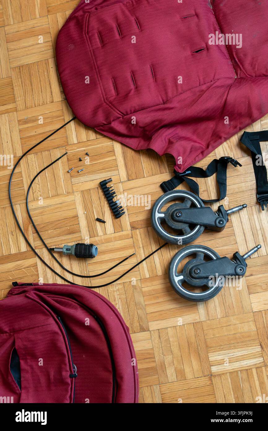 Gebrauchter Kinderwagen auf dem Boden zerlegt, während ein Mann Räder und Stoff für die Restaurierung vorbereitet Stockfoto