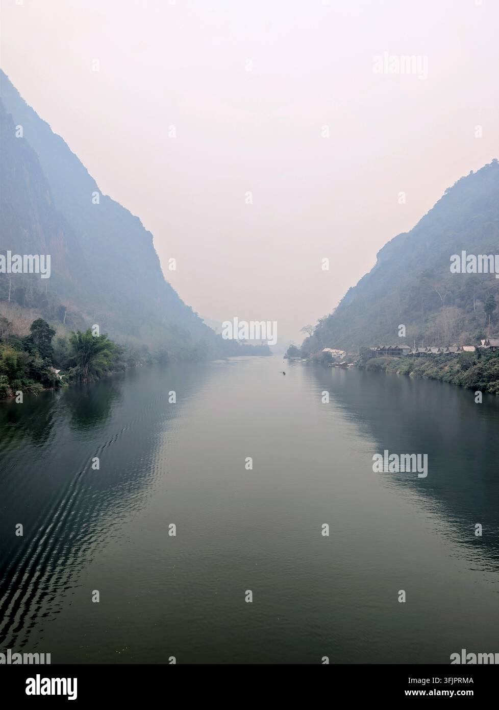 Atmosphärische Landschaftsansicht des Nam Ou-Flusses, flankiert von hohen, dschungelbedeckten Kalkstein-Karstbergen unter einem nebligen Himmel in Nong Khiaw, Laos. - Smartphone-aufgenommenes Stockfoto