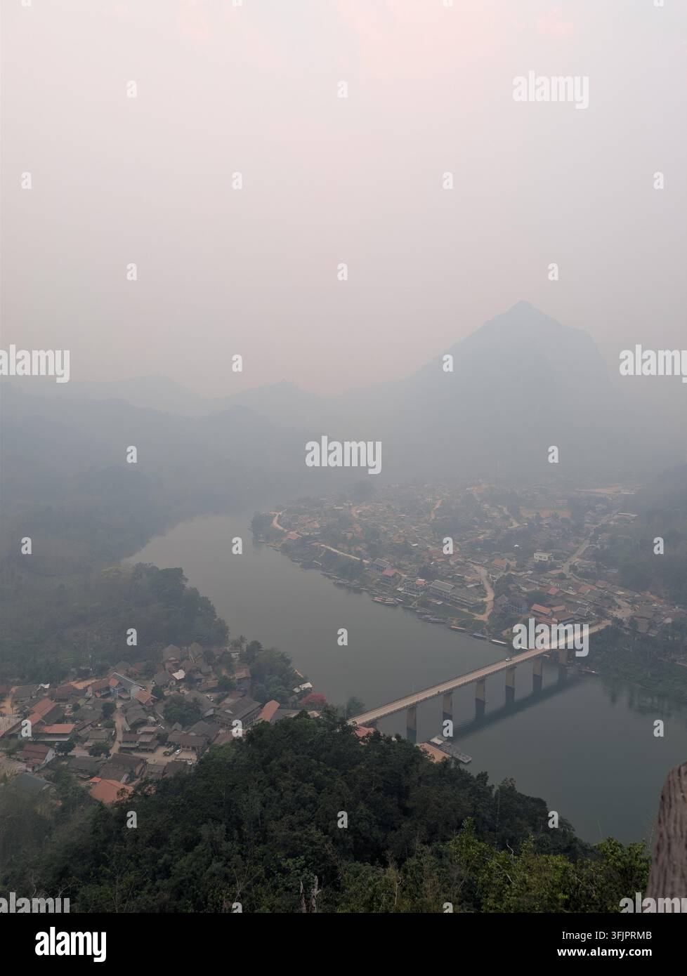 Panoramarische erhöhte Ansicht des Dorfes Nong Khiaw, umgeben von Flussbiegung, Betonbrücke und nebligen Bergsilhouetten im Norden von Laos. - Smartphone-aufgenommenes Stockfoto