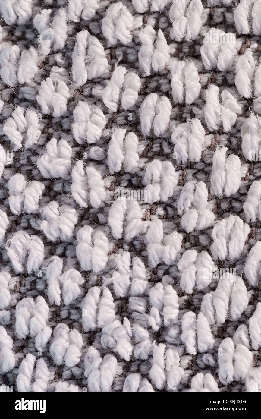 Nahaufnahme von weißem Schlingen-Garn auf grauer gewebter Textiloberfläche, zeigt weiche Fasertextur, dichtes Muster und neutralen abstrakten Hintergrund. Stockfoto