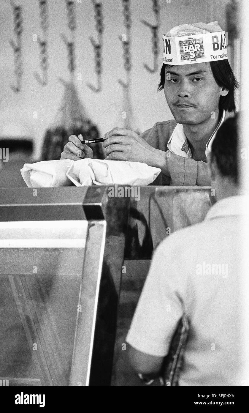 Ein Restaurant in San Francisco im Jahr 1982 zeigt einen männlichen Angestellten, der an der Theke eine Bestellung vorbereitet. Der Mann, der ein Bandana und eine Uniform trägt, wird dabei gesehen, wie er auf einen Zettel schreibt, während der Reflexion eines Kunden hinter der Theke sichtbar ist. Diese Szene wirft einen Blick auf das tägliche Leben und die kommerzielle Aktivität der Stadt in den frühen 1980er Jahren. San Francisco, San Francisco County, Kalifornien, USA Stockfoto