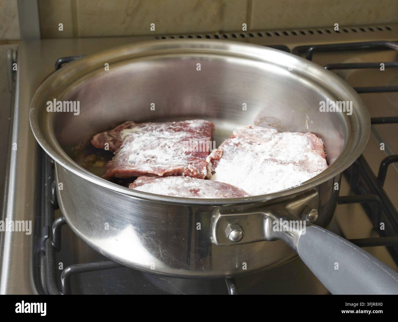 Rindfleischsteak, das in Mehl gewendet und in eine Pfanne gelegt wurde, zeigt die Zubereitung von Speisen, Panieren, hausgemachte Küche und traditionelle kulinarische Techniken. Stockfoto