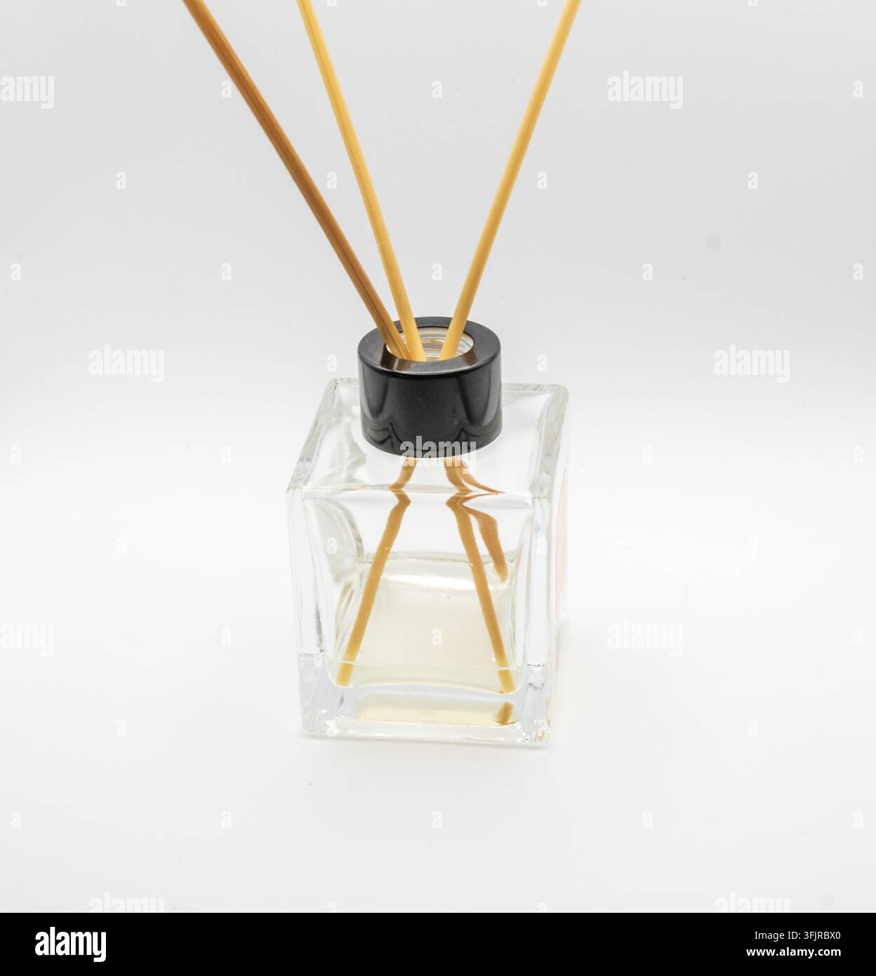 Minimaler Heimduft-Rohrstabdiffusor mit Holzstäbchen in einer transparenten quadratischen Flasche auf einem sauberen weißen Hintergrund. Stockfoto