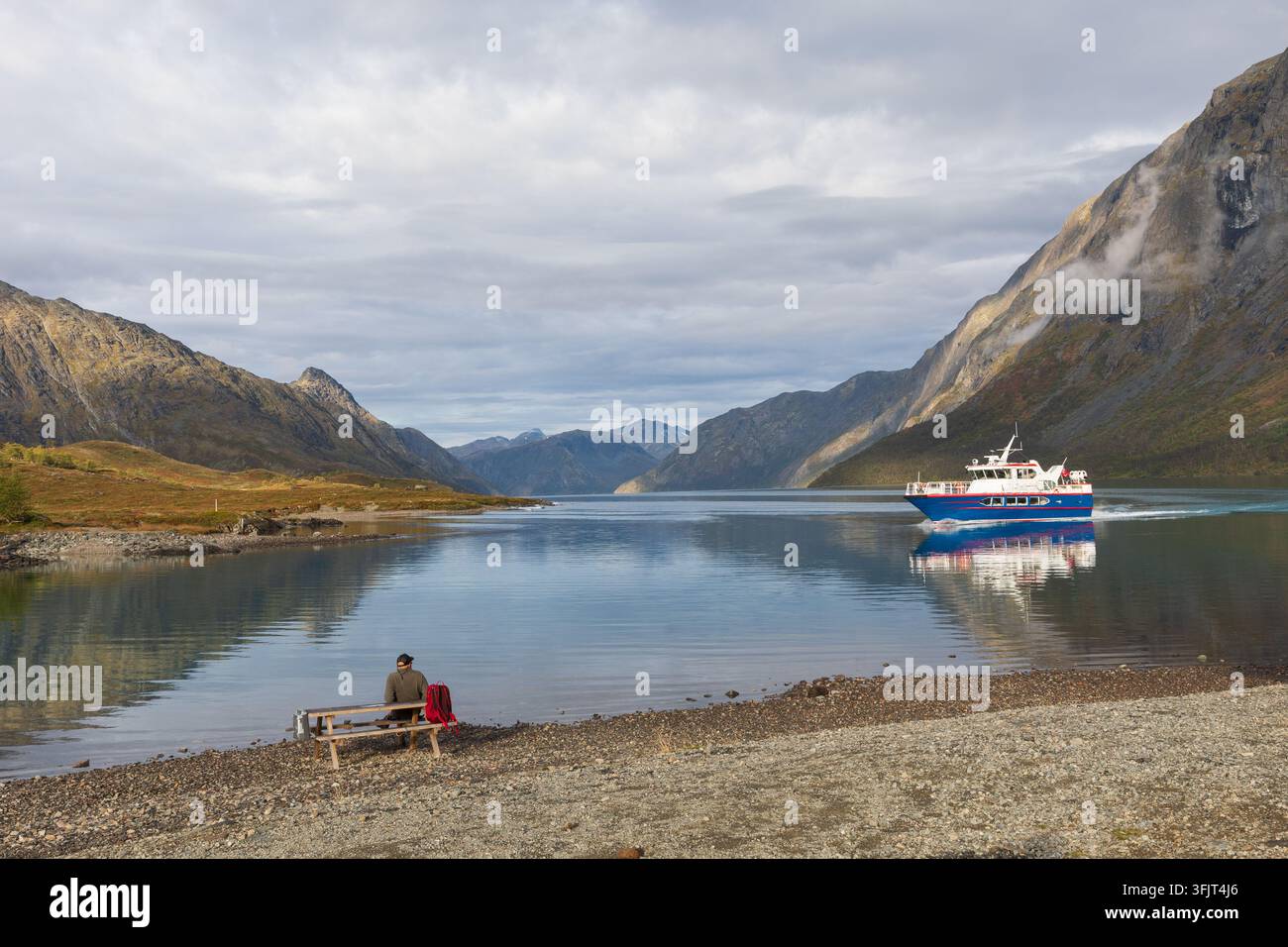 Gjende-Boot überquert den See Gjende in Gjendesheim in Jotunheimen, Norwegen, während ein Wanderer am Ufer ruht. Gjendesheim ist ein beliebter Ausgangspunkt für die Stockfoto
