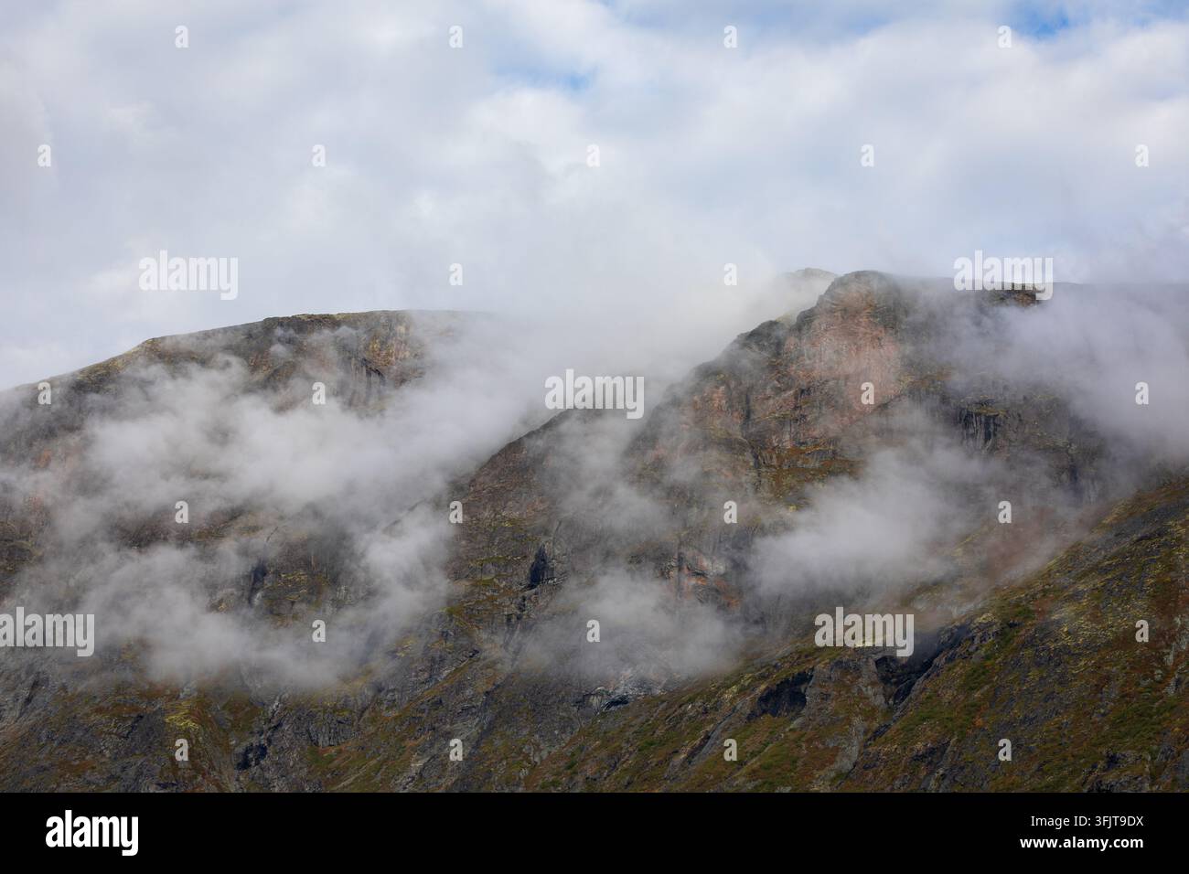 Niedrige Wolken und Nebel, die über Bergklippen in Jotunheimen, Norwegen, ziehen Stockfoto