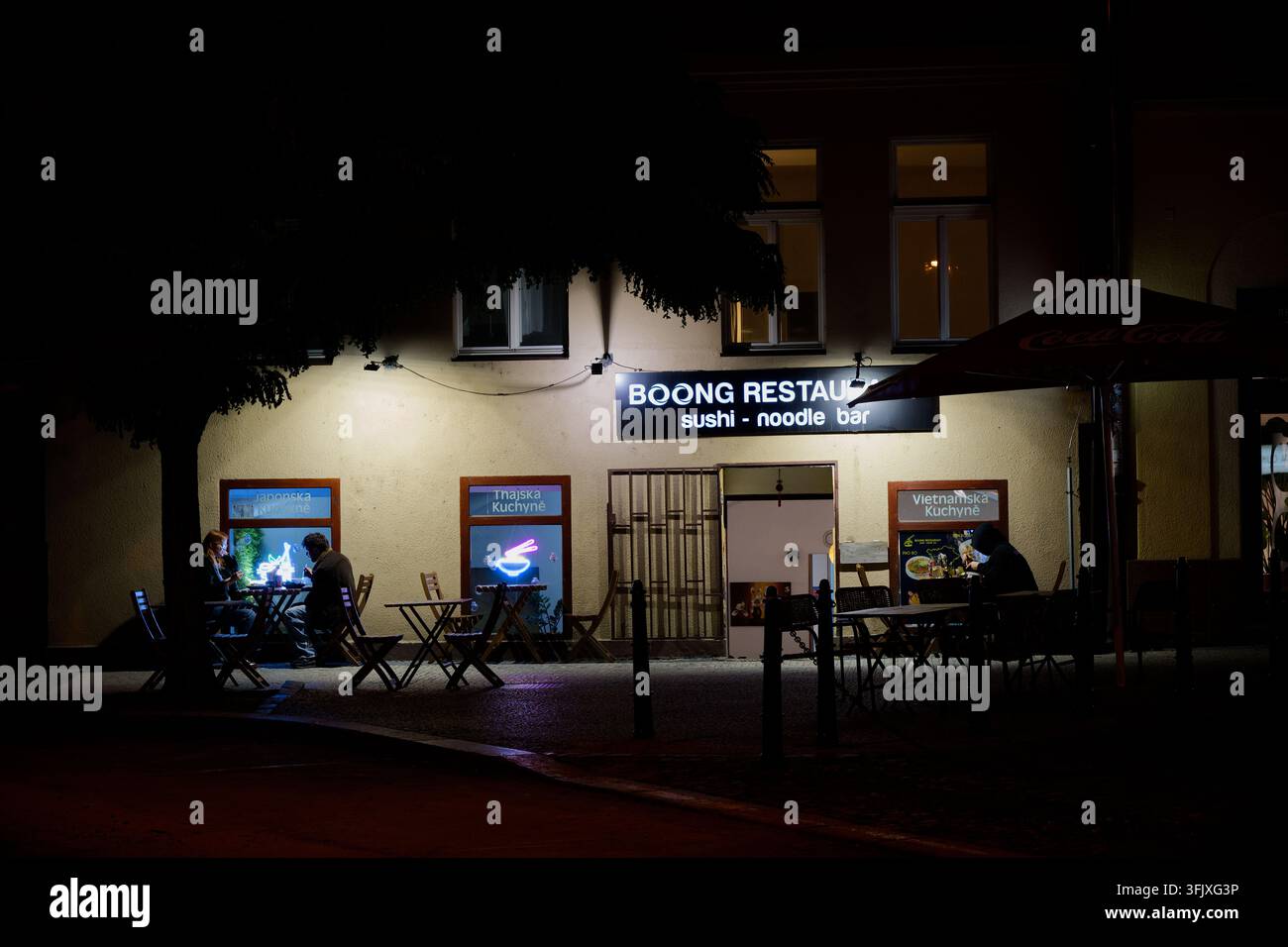 Nachtansicht des BOQNG Restaurants, einer Sushi- und Nudelbude mit draußen sitzenden Gästen. Stockfoto