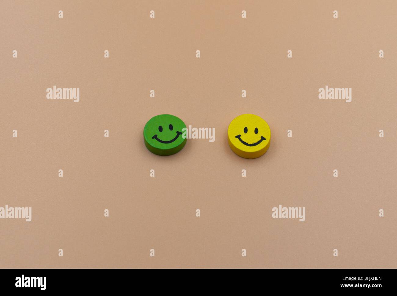 Grüne und gelbe hölzerne Smiley-Gesichter auf beigem Hintergrund Stockfoto