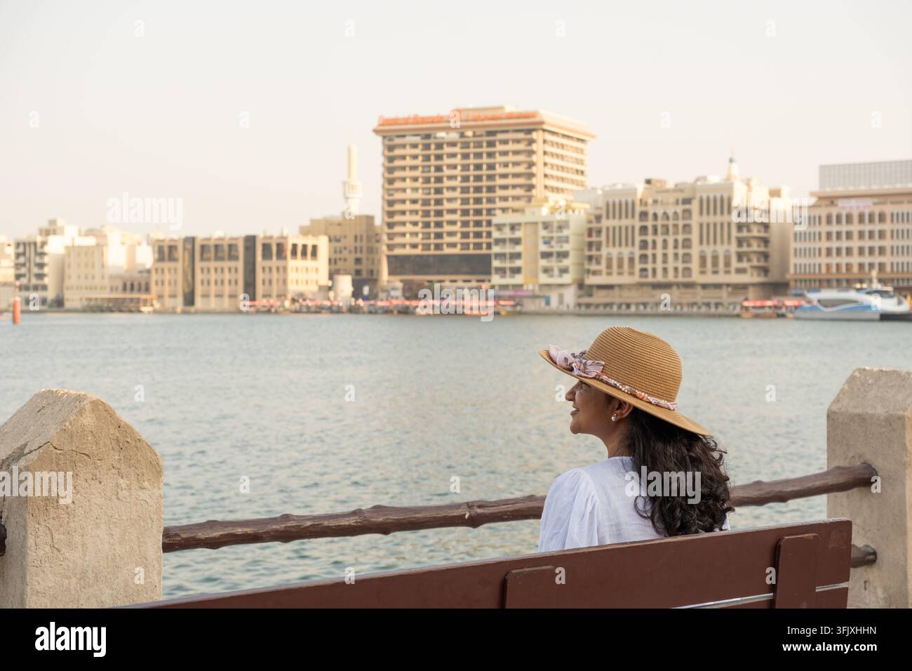 Frau entspannt sich am Ufer des Dubai Creek mit historischen Gebäuden von Deira und traditionellen Booten im Hintergrund Stockfoto