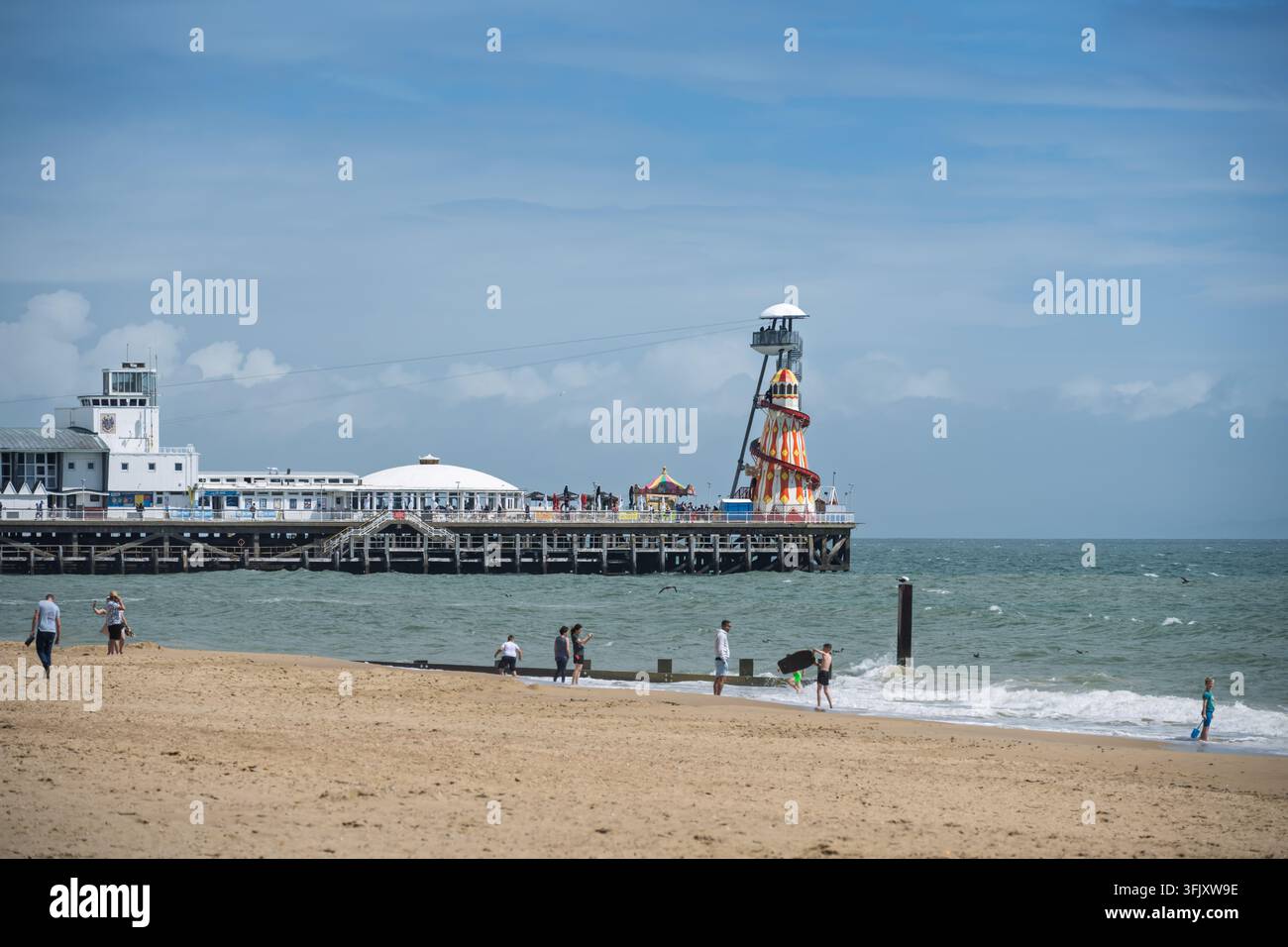 Ein weitläufiger Blick auf Touristen am Sandstrand, die in Richtung des historischen Bournemouth Piers und seiner Helter Skelter Attraktion in Dorset, England, UK blicken Stockfoto