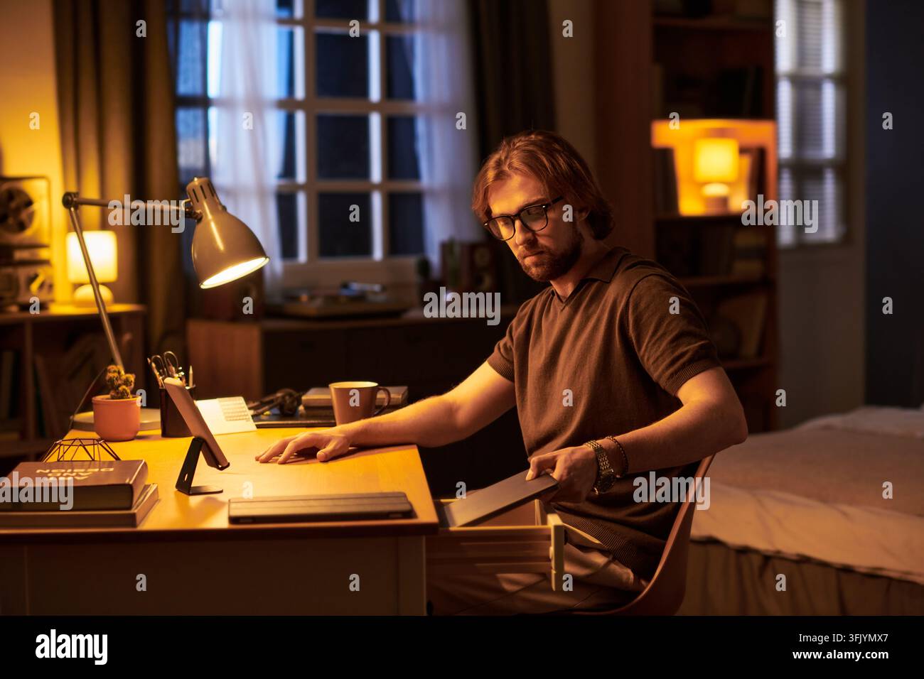 Mann organisiert den Schreibtisch, während er nachts aus der Ferne arbeitet Stockfoto