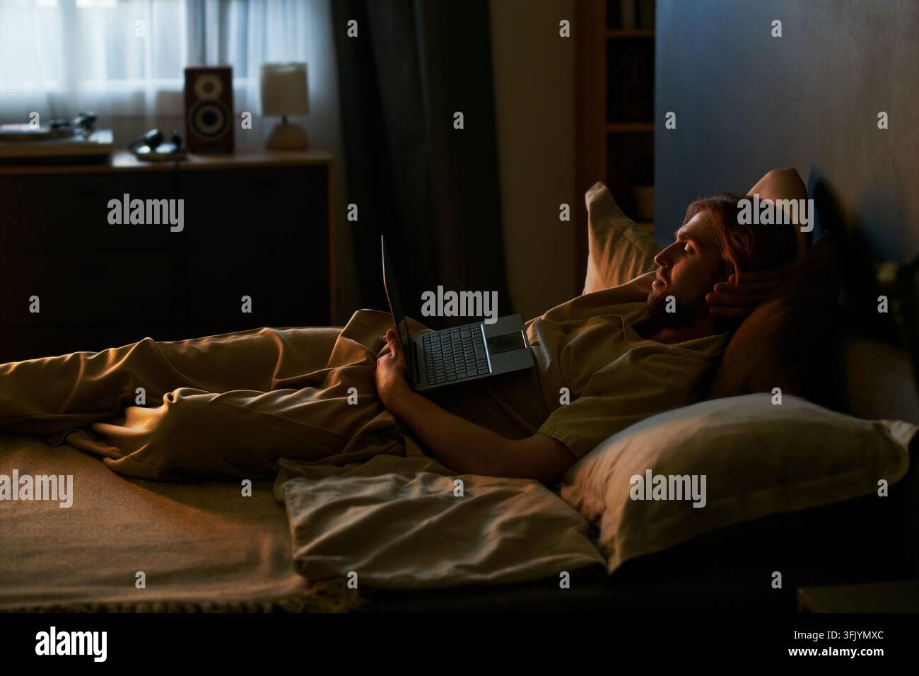 Mann ruht sich im Bett aus und schaut einen Film auf dem Laptop zu Hause an Stockfoto