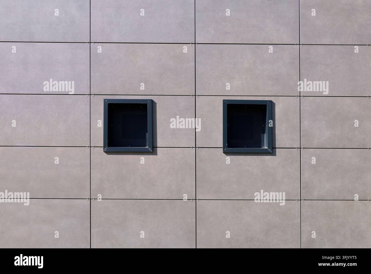 Braungraue Keramikfliesen-Ventilationsfassadenverkleidung mit zwei kleinen schwarz gerahmten Fenstern. Hintergrund und Textur. Stockfoto