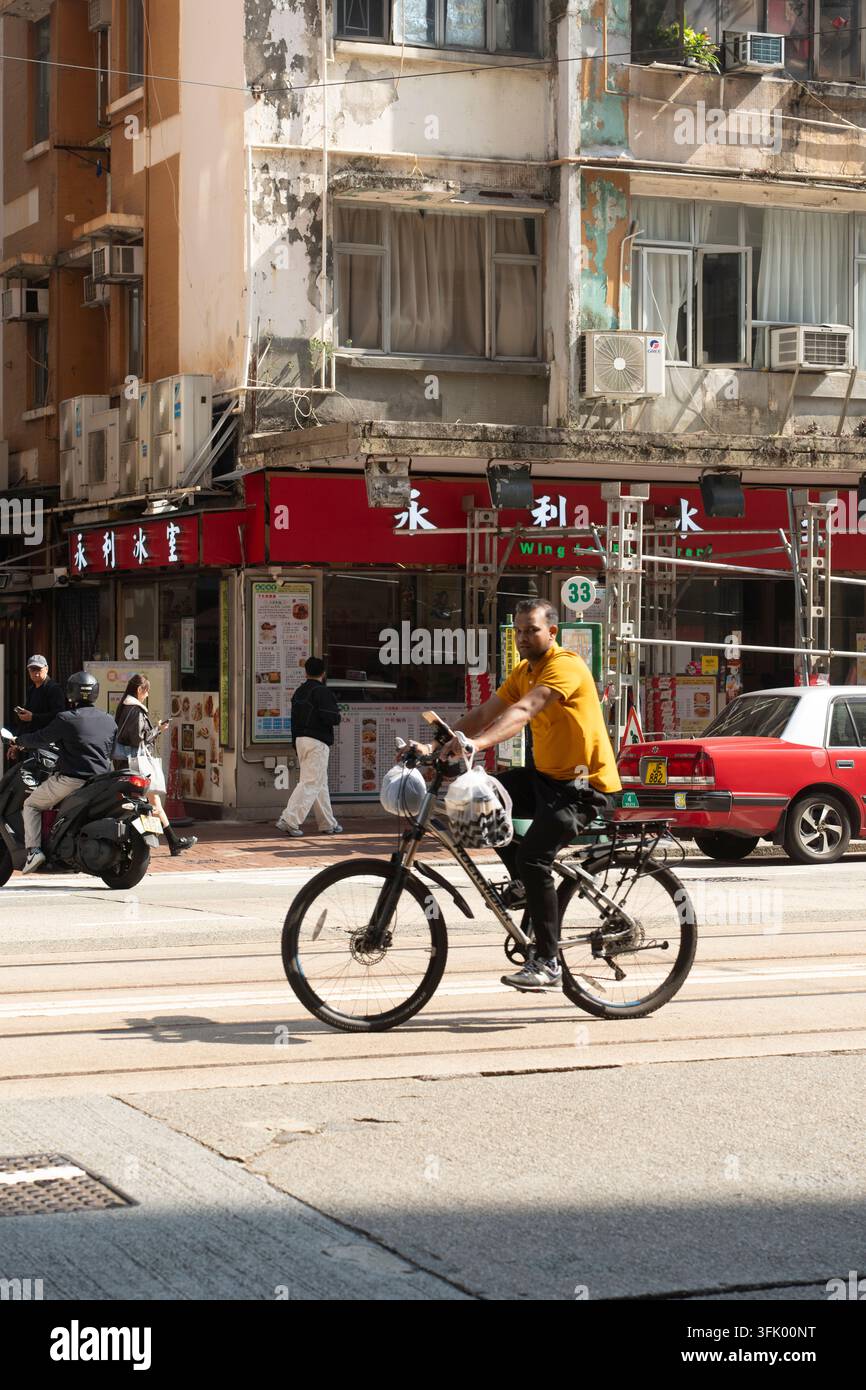 Ein Mann erledigt Besorgungen, fährt mit dem Fahrrad am Wing Lee Ice Room in North Point, Hongkong, vorbei und trägt dabei Lebensmittel. Stockfoto