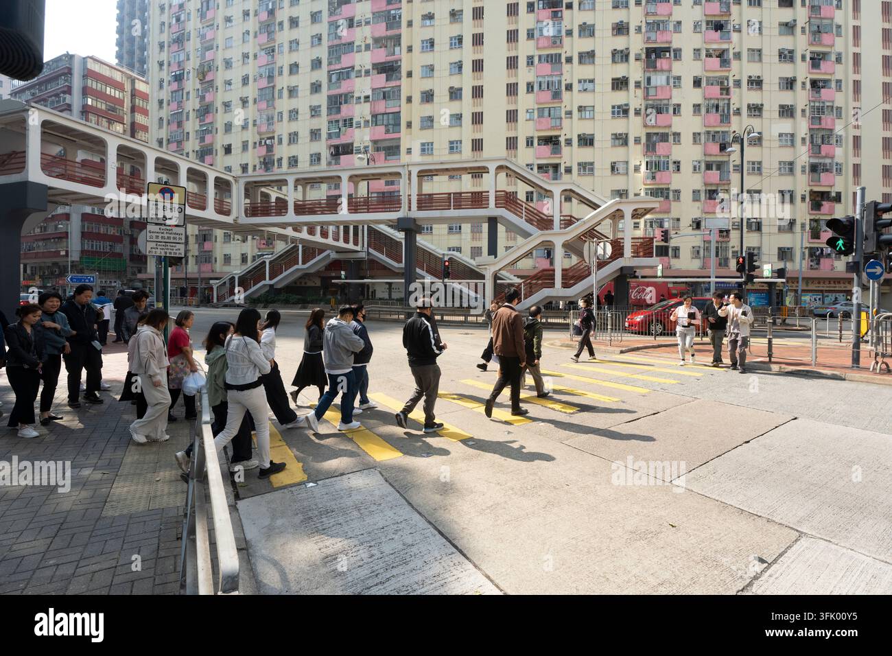Fußgänger überqueren die King's Road an einem Zebrastreifen unter den ikonischen Fußgängerbrücken von North Point in Hongkong, um durch die dichten städtischen Straßen zu navigieren. Stockfoto