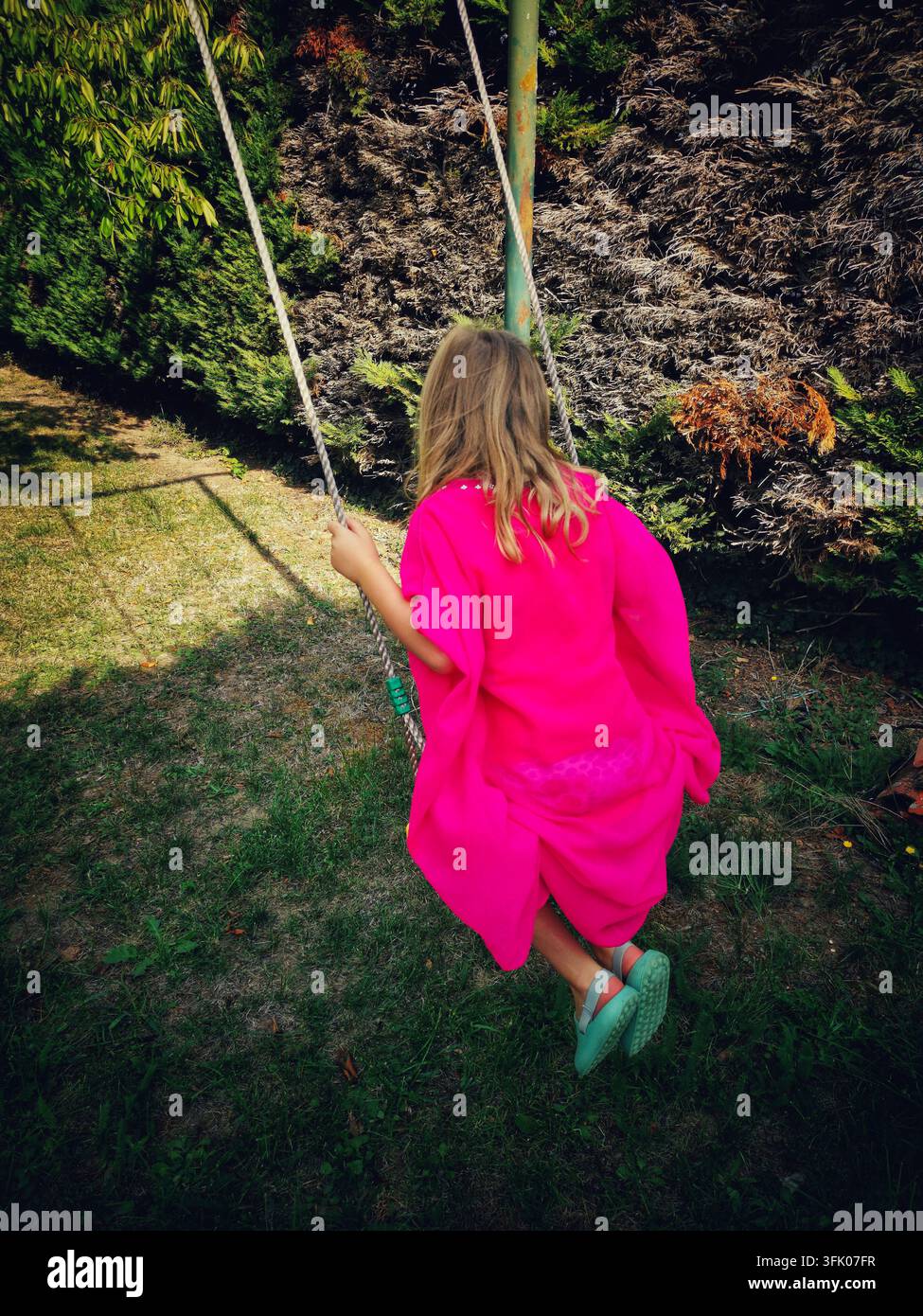 Mädchen schwingt in einem Garten an einem sonnigen Nachmittag - Smartphone-aufgenommenes Stockfoto
