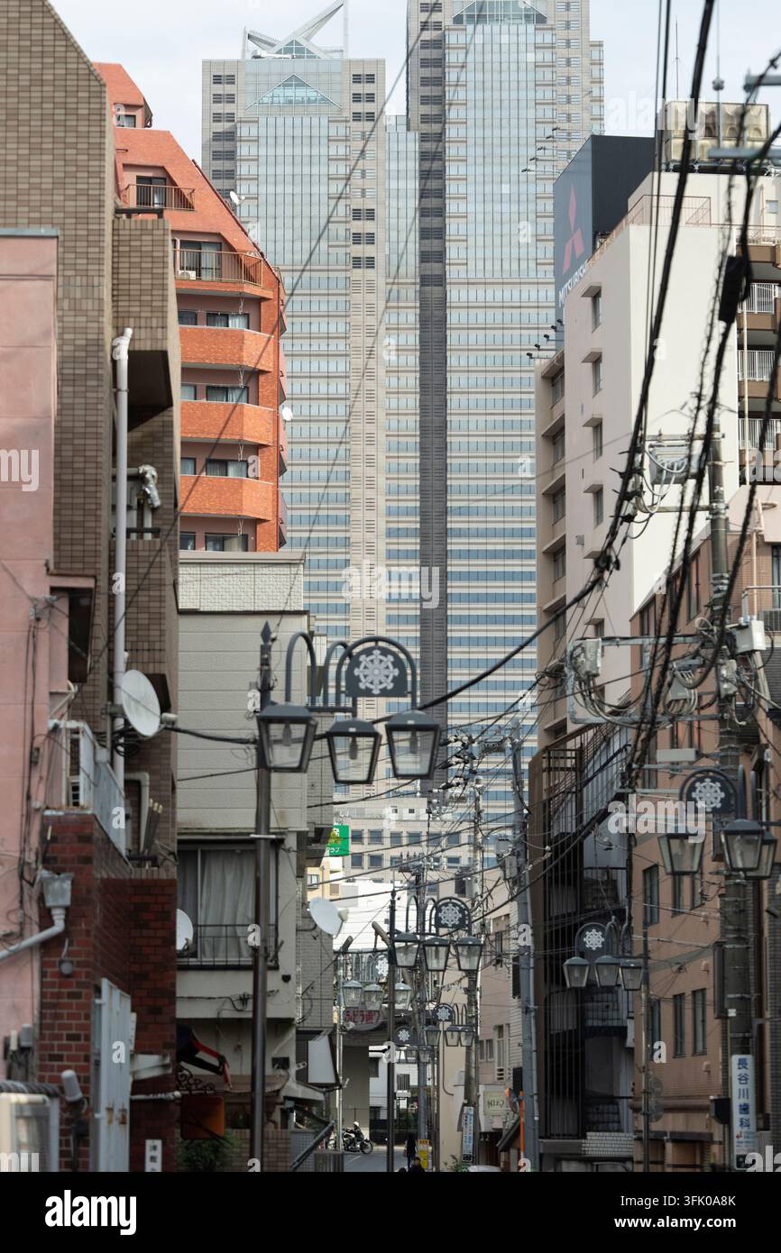 Tokyos Shinjuku Park Tower ragt über eine schmale Straße, die in Überkopfkabeln verwickelt ist, und stellt das lokale Leben in Kontrast zur futuristischen Architektur. Stockfoto