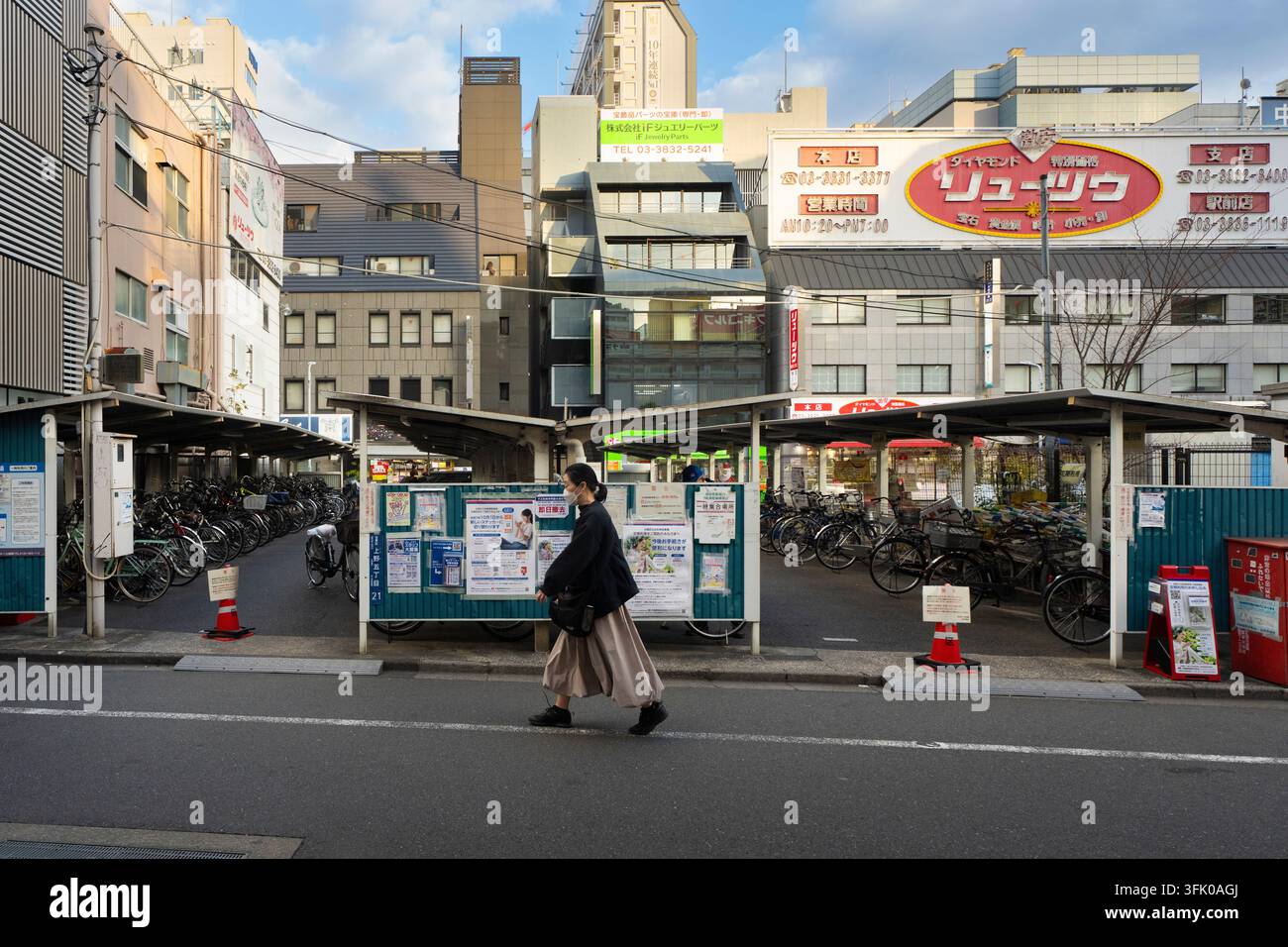 Eine maskierte Frau geht an einem Fahrradparkplatz im Ueno 5-chome-Juwelenviertel von Tokio vorbei und pendelt durch das städtische Viertel. Stockfoto