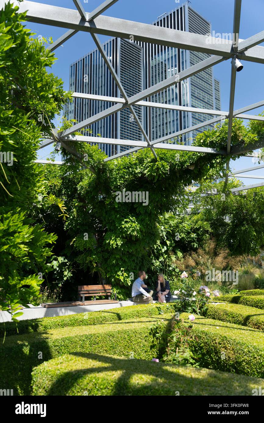 Ein Paar entspannt sich auf einer Bank im The Garden at 120, einem Dachpark in London, und genießt eine Pause mitten in üppiger Grünfläche und Stadthochhäusern. Stockfoto