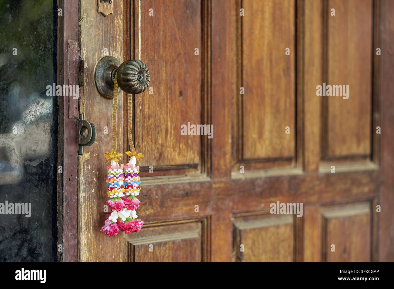 Traditioneller thailändischer Blumengirlande mit goldenen Bändern hängt an einem alten Messingtürknauf und symbolisiert Glück und Segen. Stockfoto