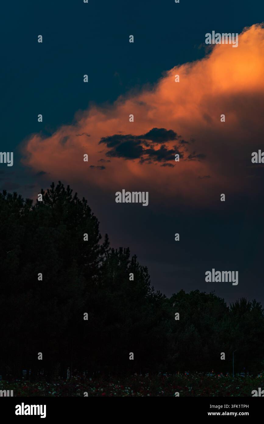 Dramatischer Sonnenuntergangshimmel mit dunklen Gewitterwolken, die lebendige orange und rote Wolken überlagern. Stockfoto