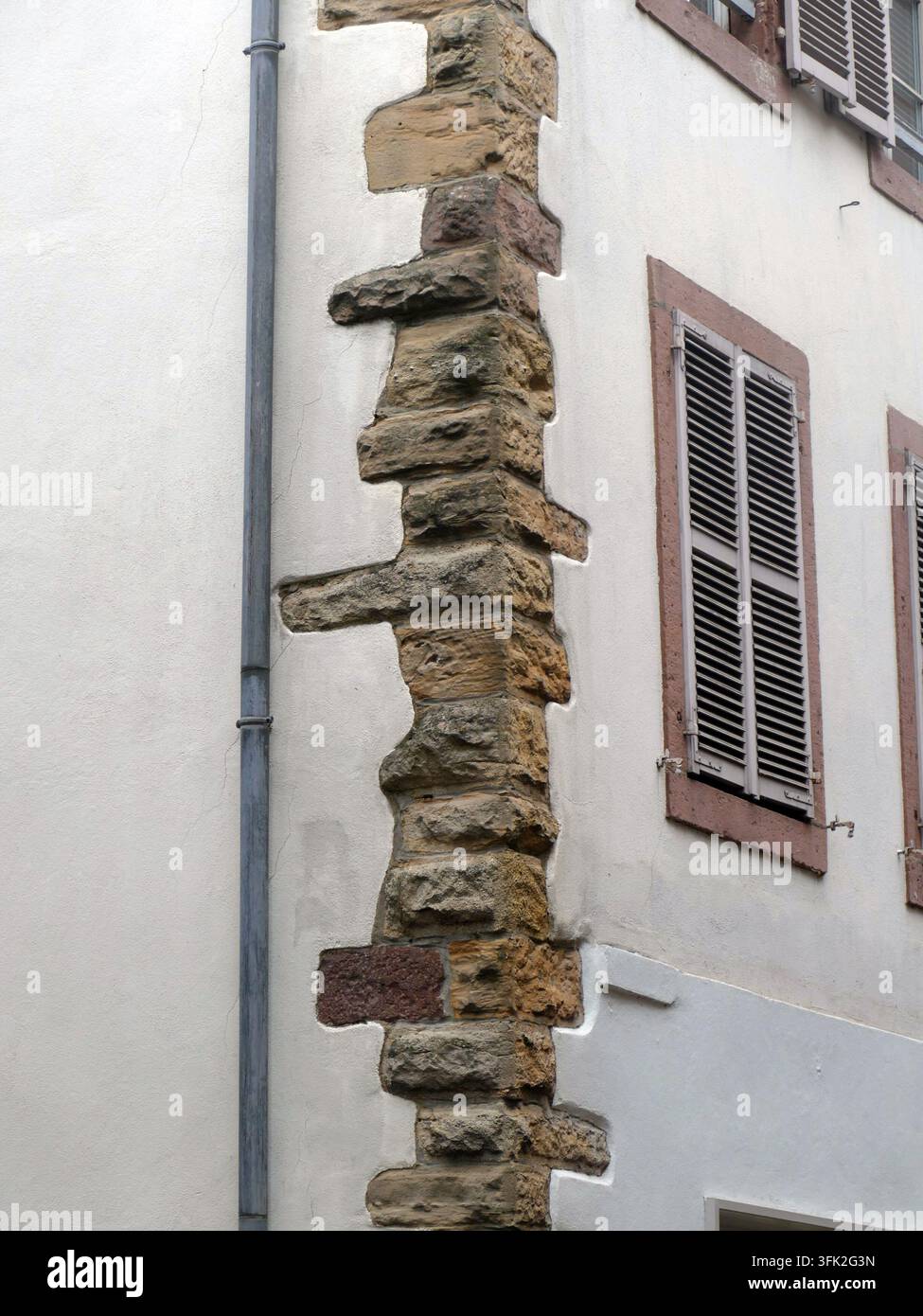 COLMAR, DEUTSCHLAND - 28. MAI 2024 - Kettenrustizierter Gebäudeeck, der eine glatte weiße Fassade, geschlossene Holzläden, die einen traditionellen Bogen betonen, kontrastiert Stockfoto