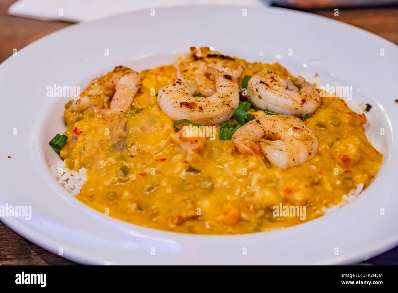 Fettige gegrillte Garnelen ruhen auf einem Bett aus herzhafter gelber Currysauce, serviert über weißem Reis in einer weißen Schüssel. Stockfoto