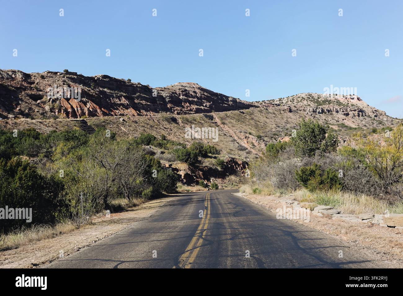 Prachtvolle Straße durch den Palo-Duro-Canyon in Texas unter klarem blauem Himmel. Reisehintergrund für amerikanische Landschafts-Wüsten-Natur-Roadtrip. Stockfoto