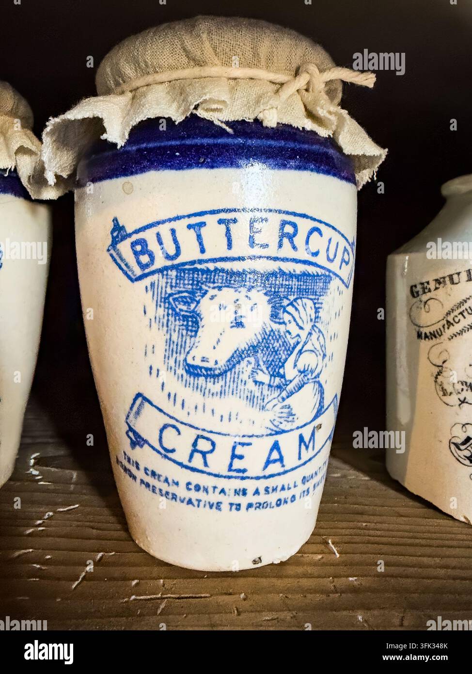 Vintage weißes und blaues Buttercup-Cream-Keramikglas mit Stoffdeckel, das auf einem Holzregal steht Stockfoto