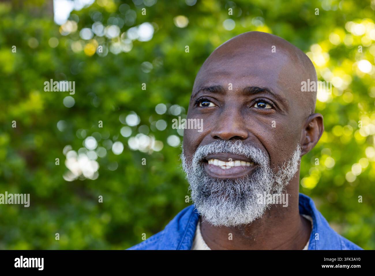 Afrikanischer Mann posiert im Park, trägt ein Denimhemd und ein helles T-Shirt, blickt nach oben rechts Stockfoto