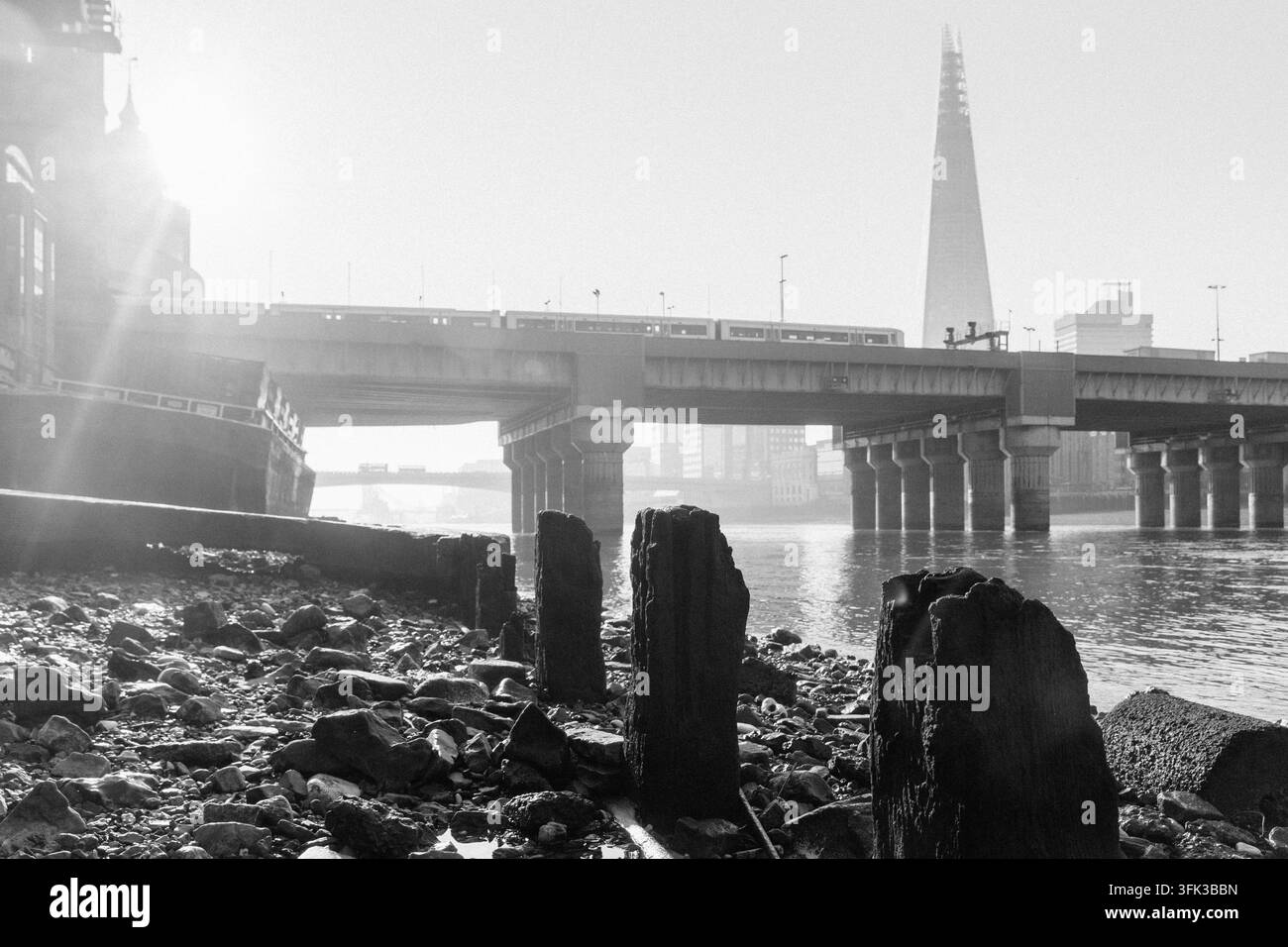 Ein Zug überquert die Cannon Street Railway Bridge über die Londoner Themse, während das Sonnenlicht auf den berühmten Shard in der Ferne trifft. Stockfoto