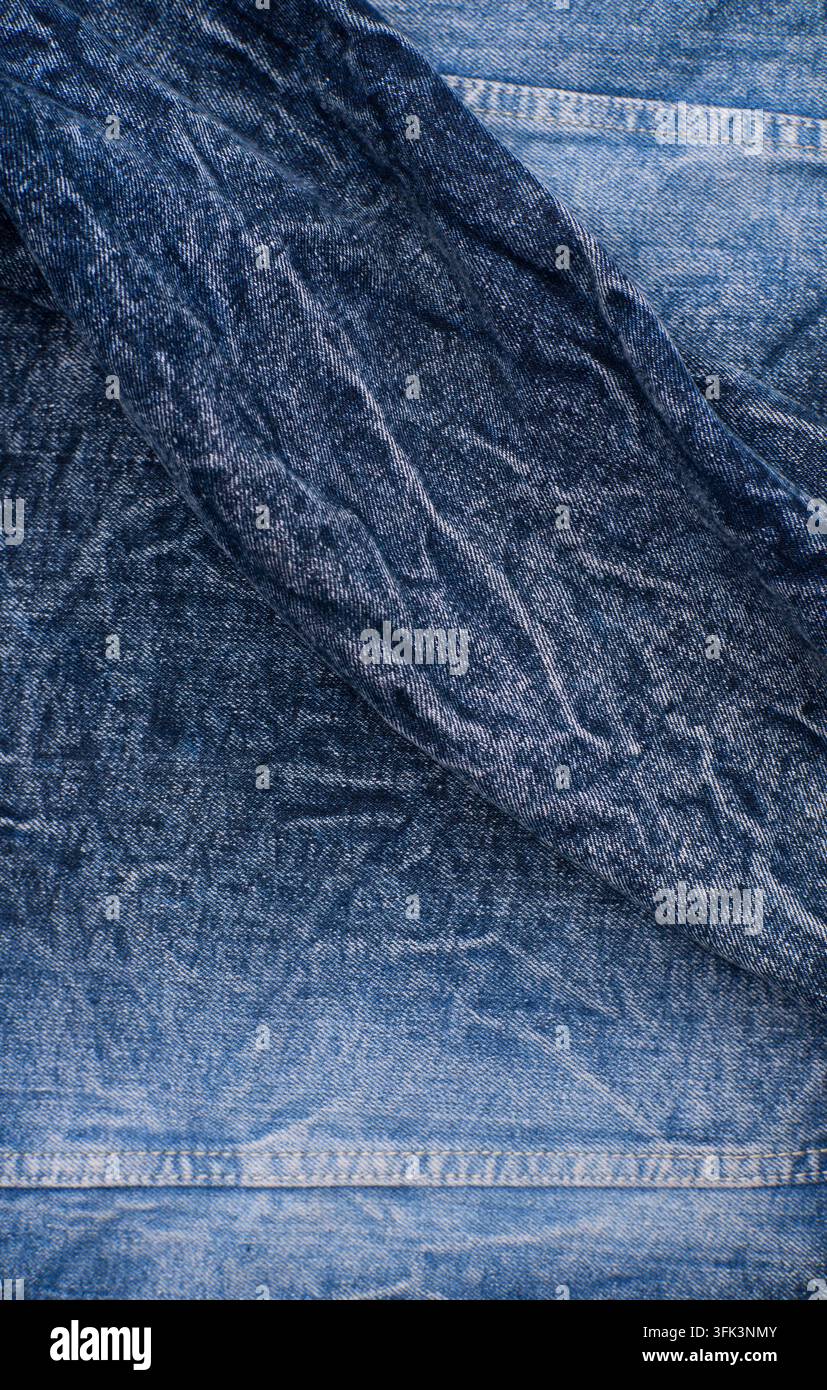 gefalteter blauer Denimstoff mit sichtbaren Falten, Nähten, verblassten Indigotönen und robuster Textur Stockfoto