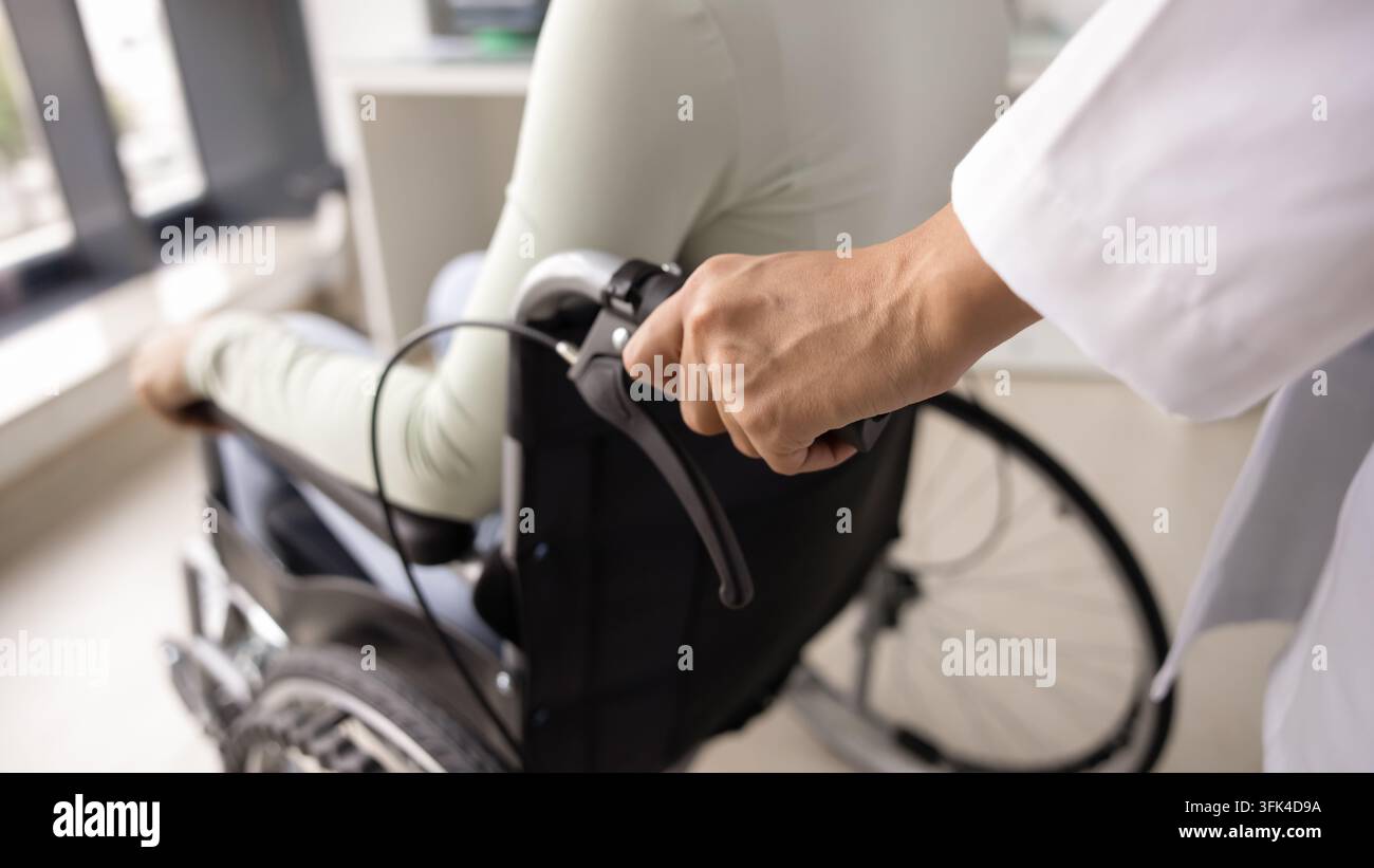 Nahaufnahme einer gekürzten Aufnahme der Hände einer Ärztin, die einen Rollstuhl schiebt Stockfoto