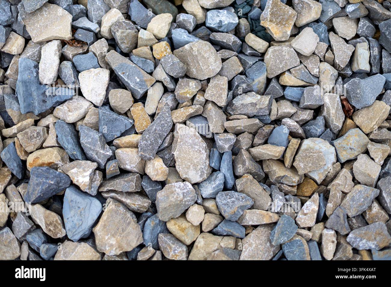Nahaufnahme-Textur aus gemischten grauen und beigen Kiessteinen. Nahaufnahme von gemischten grauen, beigen und blauen Kiessteinen, die eine raue natürliche Steinformation bilden Stockfoto
