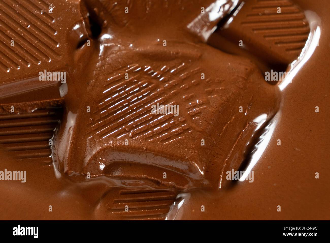 Nahaufnahme von Milchschokoladenstücken, die mit glänzender, tropfender Textur schmelzen Stockfoto