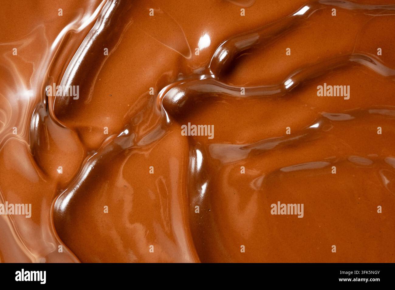 Wirbelnder geschmolzener Milchschokoladenhintergrund mit glänzender Wellenstruktur. Stockfoto