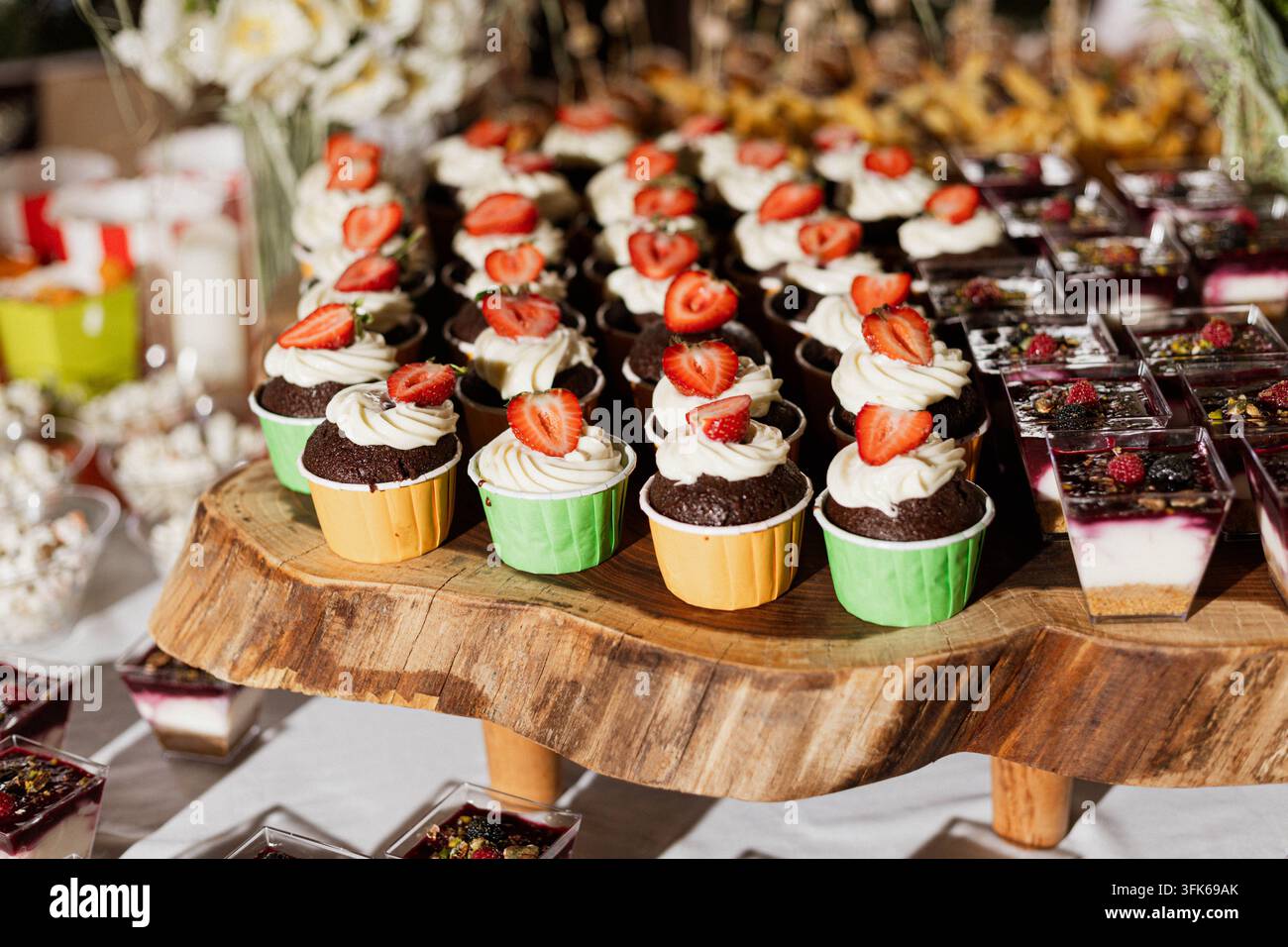 Erdbeer-bekrönte Cupcakes mit Sahneglasur und Schokoladen-Brownies, die auf Holzservierplatten für ein Dessertbuffet bei einer Veranstaltung angeordnet sind. Stockfoto
