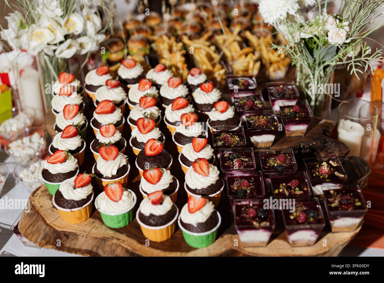 Erdbeer-bekrönte Cupcakes mit Sahneglasur und Schokoladen-Brownies, die auf Holzservierplatten für ein Dessertbuffet bei einer Veranstaltung angeordnet sind. Stockfoto