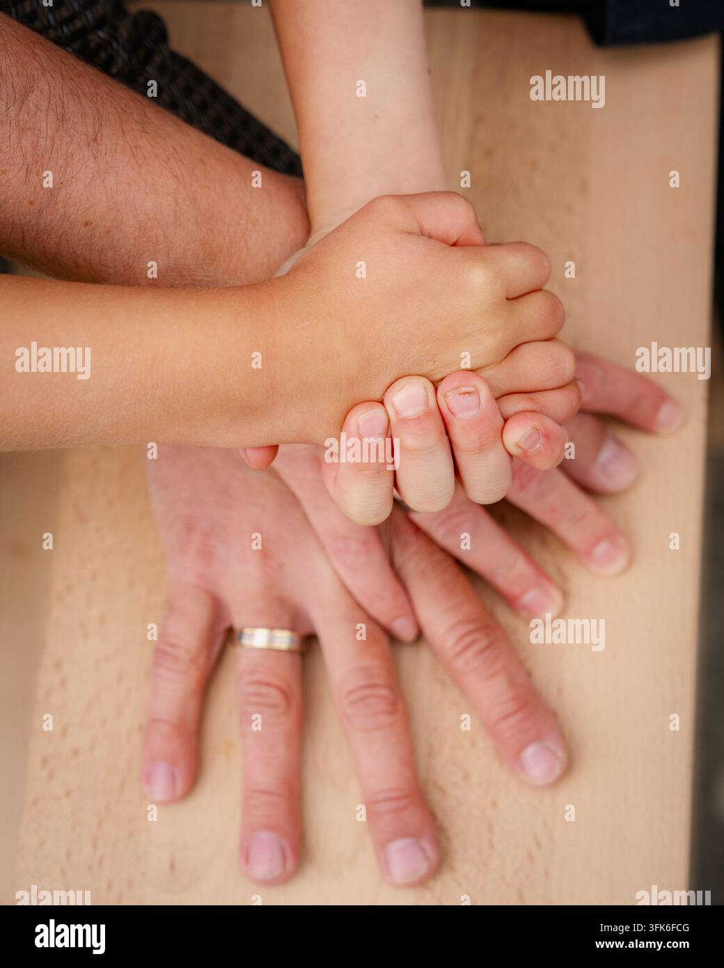 Nahaufnahme von oben einer Familie, die sich an den Händen hält, die auf einem Holztisch gestapelt sind. Konzept von Einheit, Unterstützung, Schutz, Familienwerten, Liebe und Bindung von Stockfoto