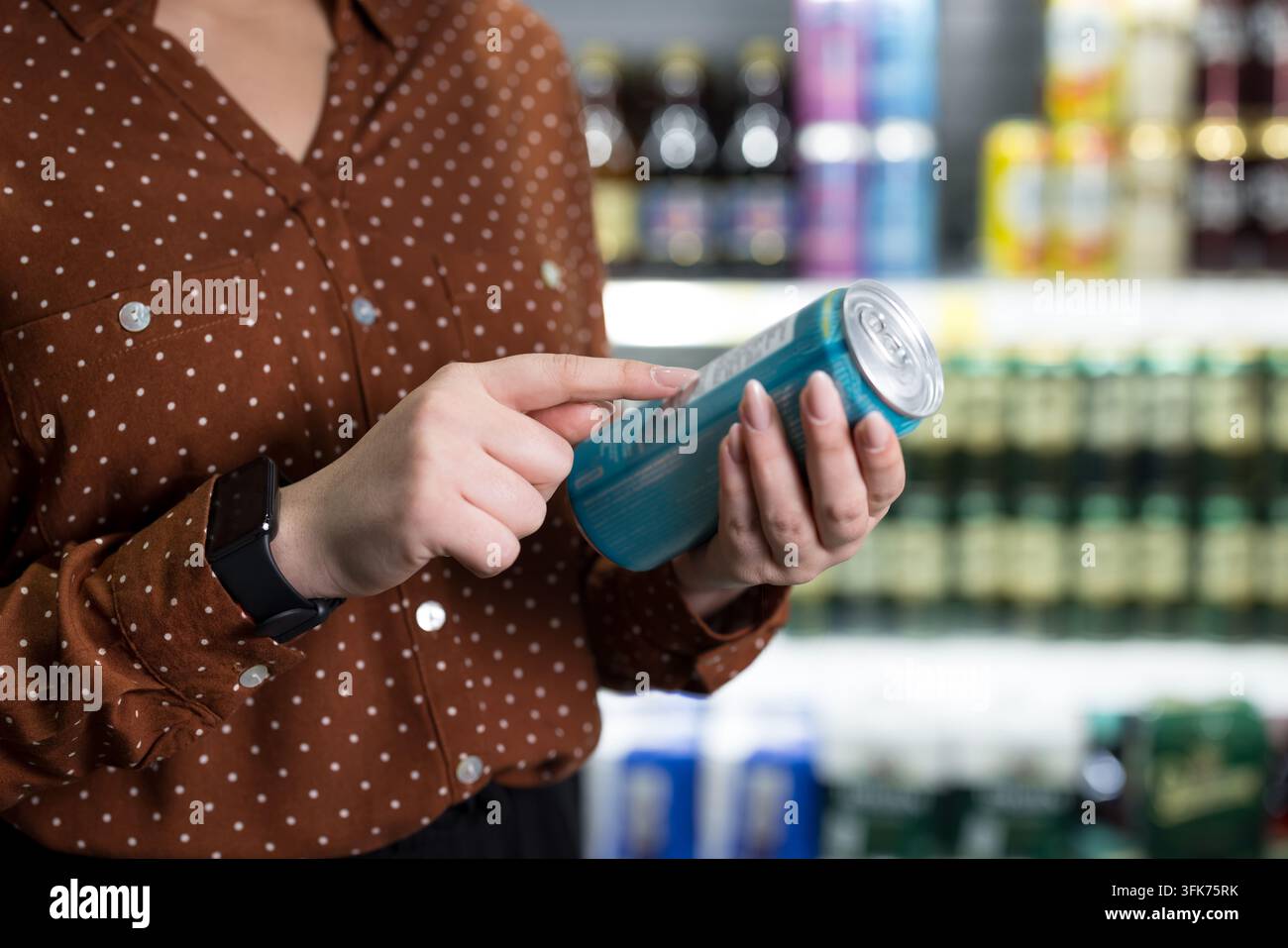 Personenhand hält eine blaue Aluminium-Getränkedose in einem Supermarktgang und liest den Nährwert- und Zutatenkasten, um eine informierte gesunde Wahl zu treffen Stockfoto