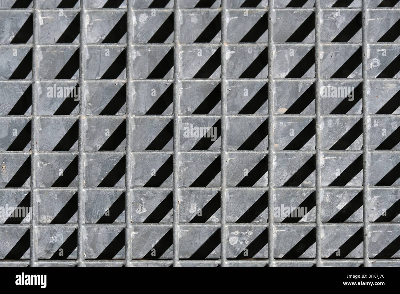 Abstraktes Muster aus Licht und Schatten auf Metallgitter mit geometrischen Mustern aus Dreiecken Stockfoto