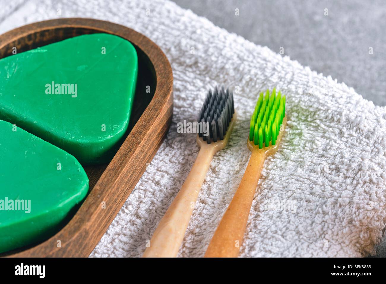 Nahaufnahme grüner dreieckiger Seife in einer Holzschale neben Bambuszahnbürsten auf einem Handtuch Stockfoto