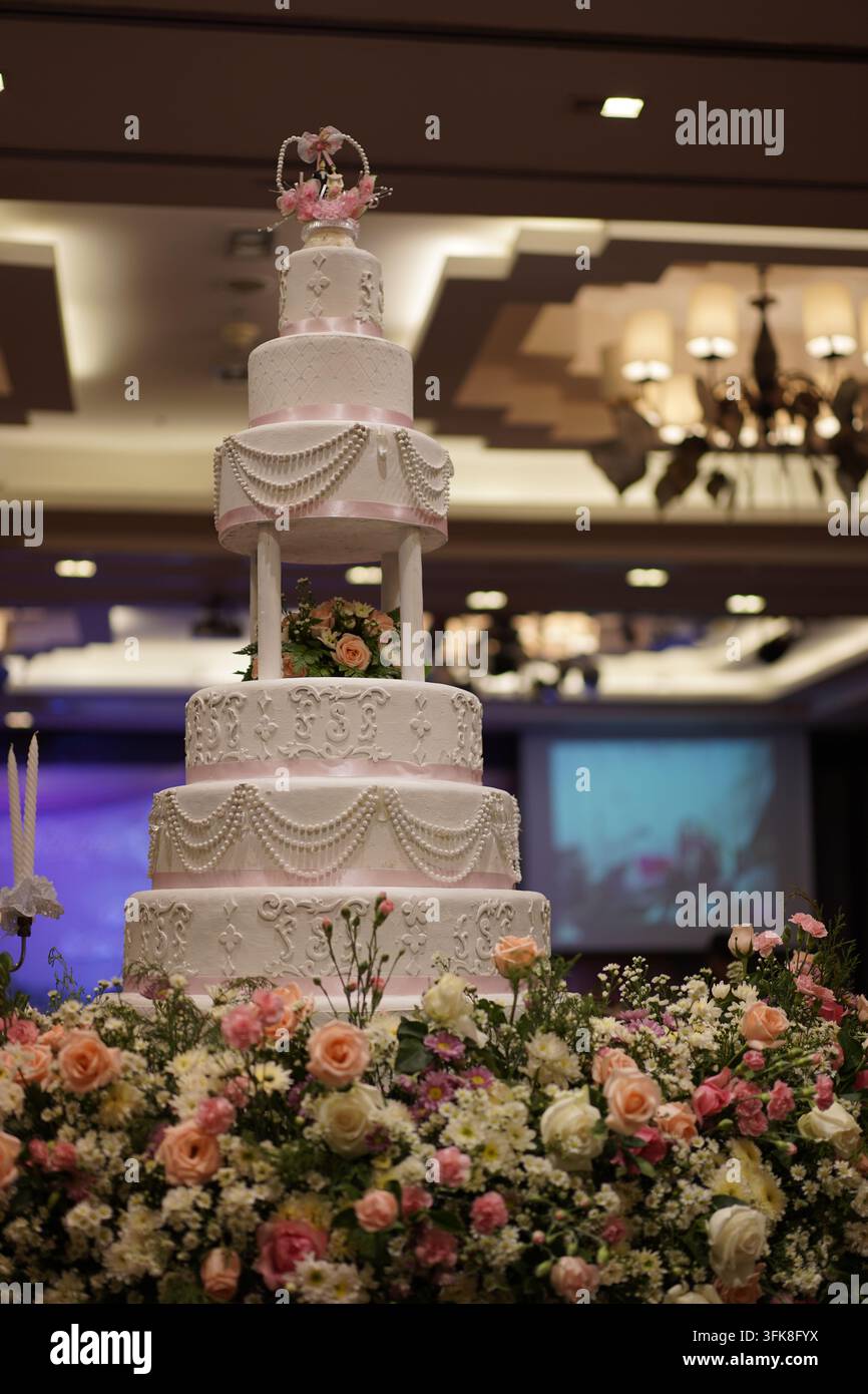 Hoher mehrstufiger weißer Hochzeitstorte dekoriert mit pinkem Band und Blumenarrangement unten Stockfoto