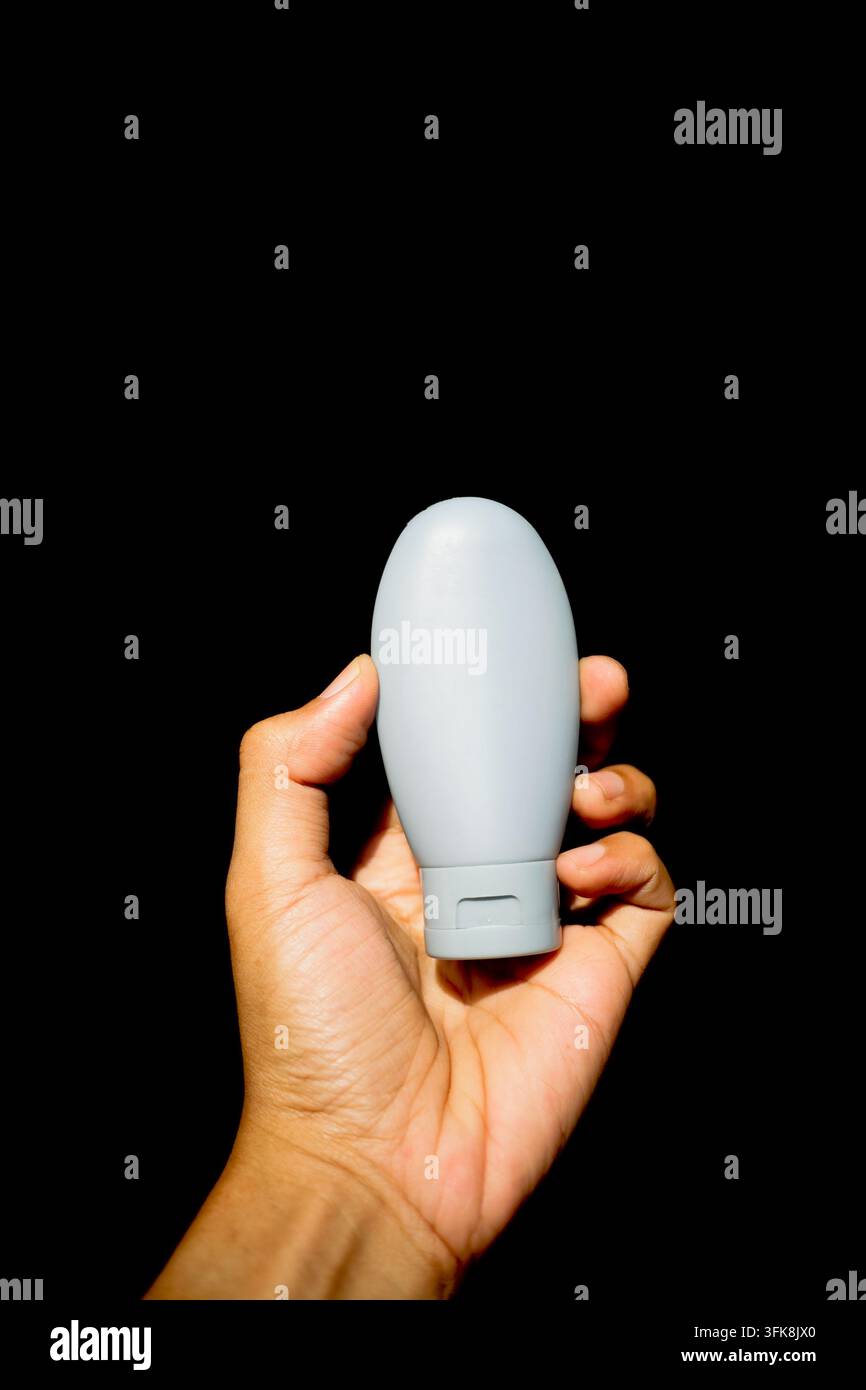 Nahaufnahme einer Hand, die eine Silikon-Reiseflasche für Kosmetika und Hygiene auf schwarzem Hintergrund hält Stockfoto