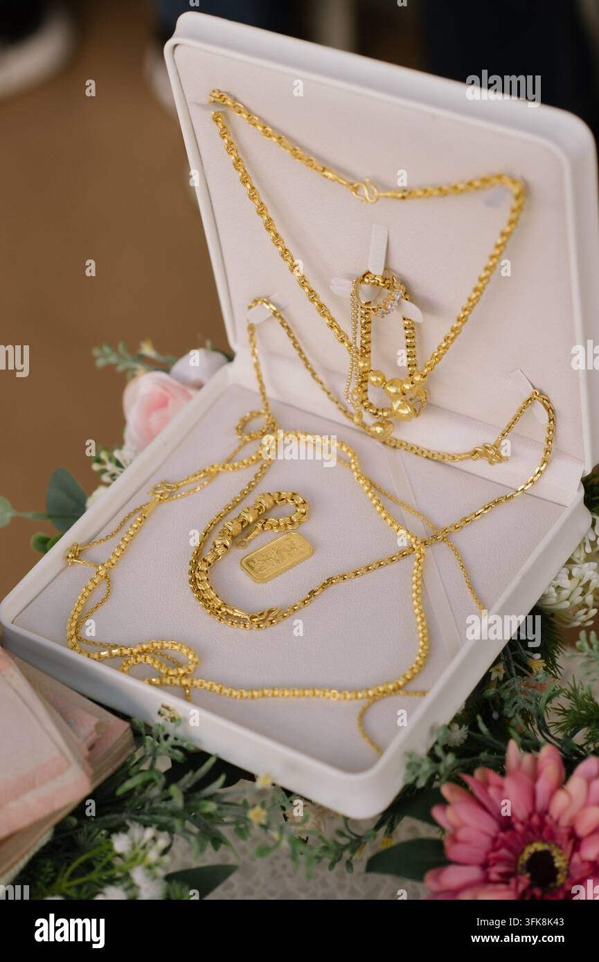 Offene weiße Schmuckschatulle mit luxuriösen Goldhalsketten und Goldbarren auf Blumenhintergrund Stockfoto