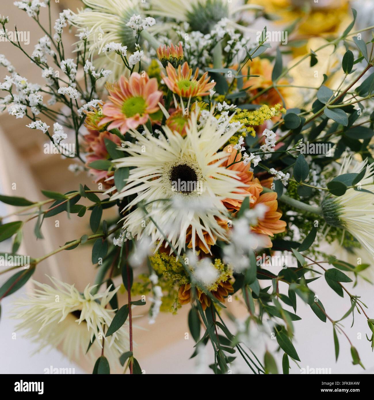 Frisches Blumenarrangement mit weißen Spinneneimerblumen, orangefarbenen Gänseblümchen und Eukalyptusblättern Stockfoto