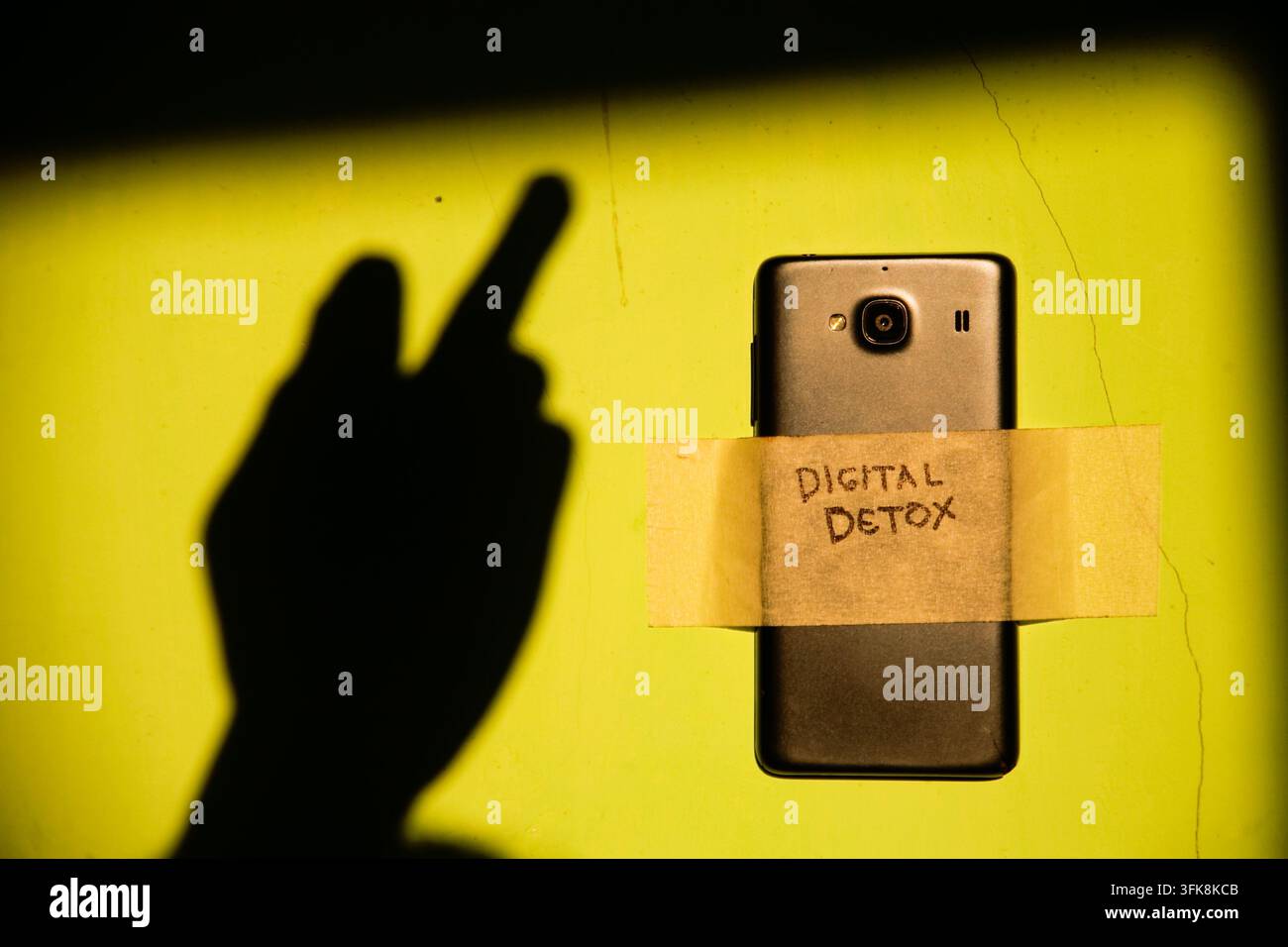 Nahaufnahme eines Smartphones, das mit dem Text „Digital Detox“ beklebt ist, und Schatten eines Mittelfingers-Handgestus auf der schmutzigen Wand Stockfoto